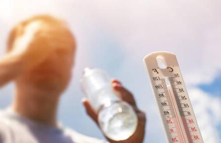 模糊的温度计图像显示温度超过华氏90度, 还有一个男人拿着一瓶水，擦着脸上的汗.